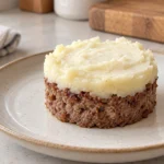 Illustration of a small cooked meat cake with plain mashed potato topping