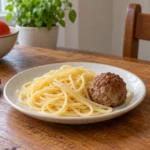 Illustration of plain spaghetti and a cooked meatball on a plate